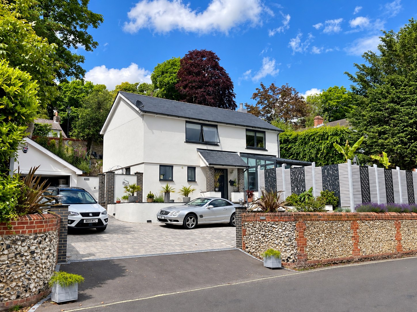 White home with dark window frames and flint boundary wall